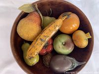 Top-down view of cherry wood bowl filled with nine glass fruit pieces including textured pear, banana, apple, persimmon, pomegranate, avocado, and other fruits