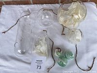 All items shown laid out on white cloth background, including five clear glass hanging vases of varied shapes with attached cords, and three colored glass spherical ornaments.