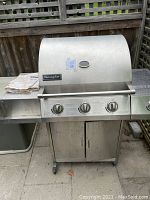 Full front view of the Charmglow gas BBQ showing the grill closed, three burner control knobs and one side burner control knob, along with front storage cabinet with double doors.