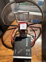 Photo showing the NBA over the door basketball hoop with transparent backboard, red rim, and white net laid flat on a table with the Skullcandy headphones box in front of it.