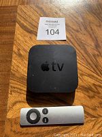 Top view of black Apple TV box with Apple logo, accompanying silver Apple remote control below it.