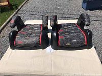 Top view of two child booster seats side by side on a beige blanket outdoors, showing seat and armrest details.