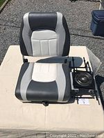 Front view of the boat seat showing the black, white, and grey vinyl upholstery and the attached metal swivel mount with clamp screws.