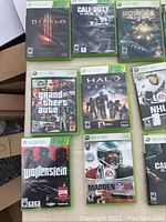 Top angle view showing 9 Xbox 360 game cases including Diablo III, Call of Duty: Ghosts, BioShock 2, Grand Theft Auto IV, Halo Reach, NHL 07, Wolfenstein: The New Order, Madden NFL 06.