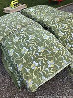 Four green outdoor lounge chair cushions with floral pattern visible from top and side, one cushion has hole damage from spark