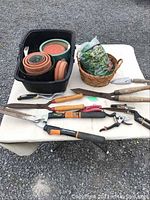 Overview of garden clippers, various clay pots, gardening mesh, and other small tools displayed on a table.