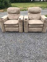 Front view of two beige theatre recliner chairs placed outdoors on gravel showing overall look, armrests with cup holders, cushions and backrests.