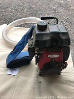 Honda Extreme transfer pump with attached blue inlet hose and transparent discharge hose laid on a cloth surface outdoors.
