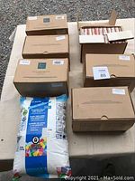Six full boxes of Winchester Tile Company ceramic tiles, unopened and stacked with a bag of grout placed in front on a table.