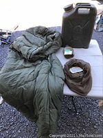 Photo showing a green cold weather sleeping bag inner liner, small container of boot polish, brown mosquito head net, and a black heavy plastic jerry can.