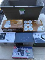 Photo showing multiple boxed lighting products and a large plastic tote with damaged lid, all unused in original packaging
