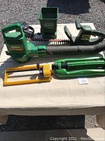 Full view of all lawn maintenance equipment on table outdoors: hedge trimmer, seed spreader, sprinkler, quick pump.