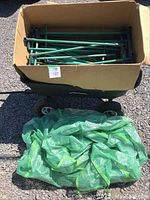 Photo shows cardboard box filled with green metal poles for greenhouse and green mesh/netting cover spread in front of box.