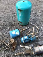 Full view of pumps and pressure tanks on gravel surface showing components and condition.