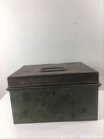Front view of vintage metal box showing handle on top, keyhole on front, and rust spots.
