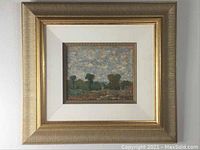 Full view of framed landscape painting with white mat and gold frame hung on wall