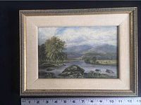 Full view of landscape painting in decorative beige and gold frame with ruler for size reference.