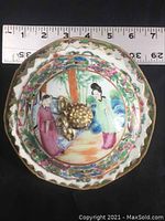 Top view of covered porcelain dish showing hand-painted Chinese figures and ruler for size reference
