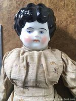 Close-up of porcelain doll's head and upper torso showing porcelain head with black hair, blue eyes, and original dress fabric