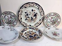 Front view of 6 porcelain plates arranged in a group showing various floral designs and shapes