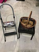 Photo showing the gray two-step ladder, dark brown wicker table, and two nested wicker baskets on a concrete floor.