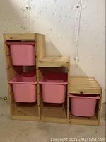 Front view of the wooden toy organizer showing five pink plastic totes in compartments.