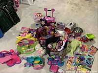 Photo showing assortment of dolls, toy vehicles, plush toys, play sets, and children's books arranged on floor.