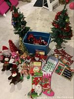 Two 4-foot artificial Christmas trees decorated with red garlands and ornaments, standing in urns with various Christmas decorations including stuffed elf dolls and holiday signs arranged nearby.