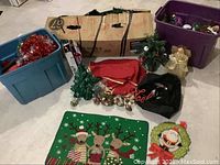 Photo showing the two large totes filled with assorted Christmas decorations, a green felt reindeer Christmas mat, and small decorative items including mini trees, angels, and a 'Noel' sign.