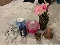 Whole lot with decorative vase, flowers, candle, food container, vaporizer, and packaged speaker on floor with carpet background