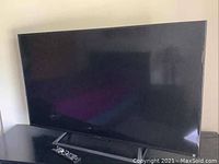 Front view of 48″ Sony TV on stand with remote control placed in front