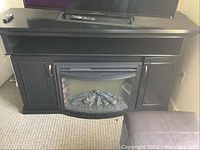 Full view of black electric fireplace unit with TV stand top, side cabinets, and electric firebox in center.
