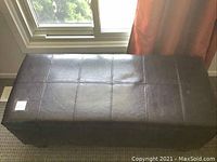 Front view of brown faux leather storage bench showing stitched top and minor marks.