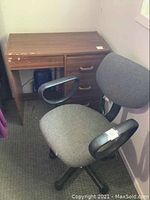 Wooden desk and grey office chair placed on carpeted floor near walls.