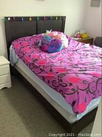 Full view of queen bed frame with dark wood headboard and white box spring base, pink and purple bedding on top (not included).