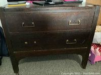 Front view of the antique wooden dresser showing three drawers with brass handles and knobs.