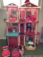 Front full view of the Barbie house showing pink and cream colors with interior furniture set up including bed, sofa, vanity, bathroom fixtures, and dining area.