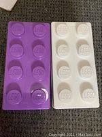 Purple and white LEGO brick-shaped storage containers on carpet.