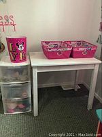 Kids table with two pink canvas storage totes and pink Minnie Mouse garbage can on top, plastic storage drawers underneath