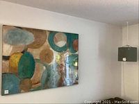 Wide shot showing large contemporary abstract painting on wall with abstract circular shapes in varied colors plus IKEA hanging light on ceiling.