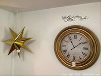 Wall clock on right with antique gold frame, Roman numerals, and adjacent hanging gold paper star light with price tags visible.