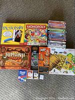 Photo of assorted board games including Pictionary, Monopoly Junior, Jumanji, Jenga, Phase 10, wooden chess/checkers set, and about 15 DVDs stacked