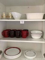Shelving with mugs (red and brown), white bowls with red stripe, white gravy boat, and white ceramic baking dish.