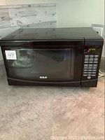 Front full view of black RCA microwave on counter with clear window and brand visible