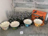 Photo showing four decorative ceramic bowls with floral patterns in various colors, seven clear stemmed wine glasses, one tall clear drinking glass, and one small clear glass cup on countertop.