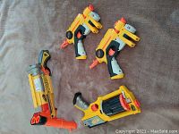 Four Nerf blasters laid on surface: two Single Shot with laser targeting, Maverick Rev-6, Barrel Break IX-2. Visible dart tips and blaster details.
