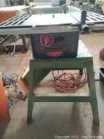 Front view of vintage Beaver 8 inch table saw on green wood base stand showing cast iron top and red control knob.