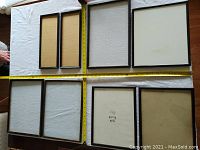 Top-down view of assorted rectangular picture frames with measuring tape showing approximate lengths, mostly in black or wood tones.