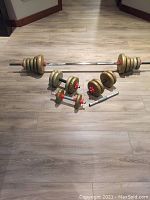 Full view of chrome barbell with gold weight plates and two dumbbell bars with plates and red star-lock collars