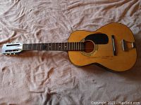 Full view of the acoustic guitar showing its natural finish, black pickguard, and six-string neck with one string missing.